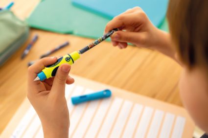 Ein Kind wechselt die Tintenpatrone seines Griffix-Füllers von Pelikan aus. Im Hintergrund ist ein Schreibtisch mit Schulmaterialien zu erkennen.